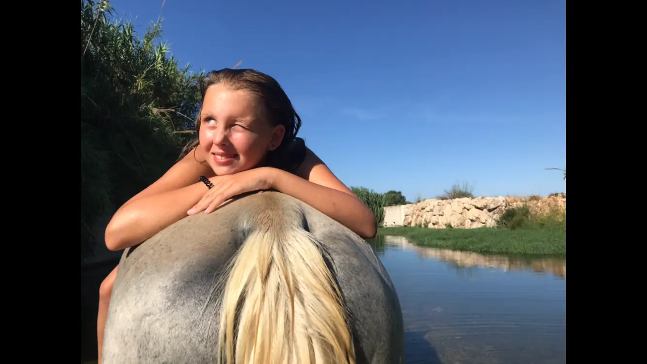 Niña bañándose en el río junto a un caballo